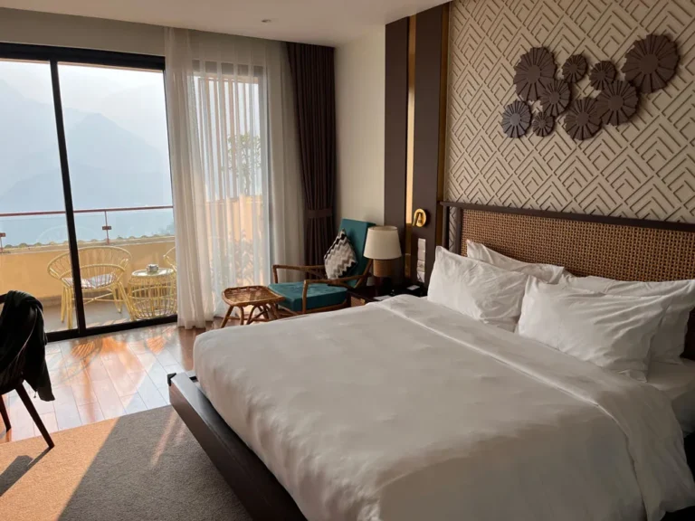 Luxury hotel room in Sapa, Vietnam, featuring a king-sized bed, stylish decor, and a balcony with a breathtaking mountain view.